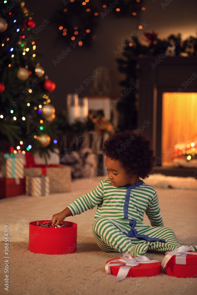 Cute African-American baby girl with gift at home on Christmas eve