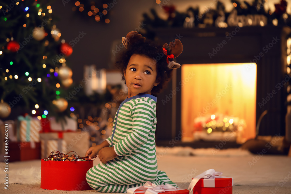 Cute African-American baby girl with gift at home on Christmas eve