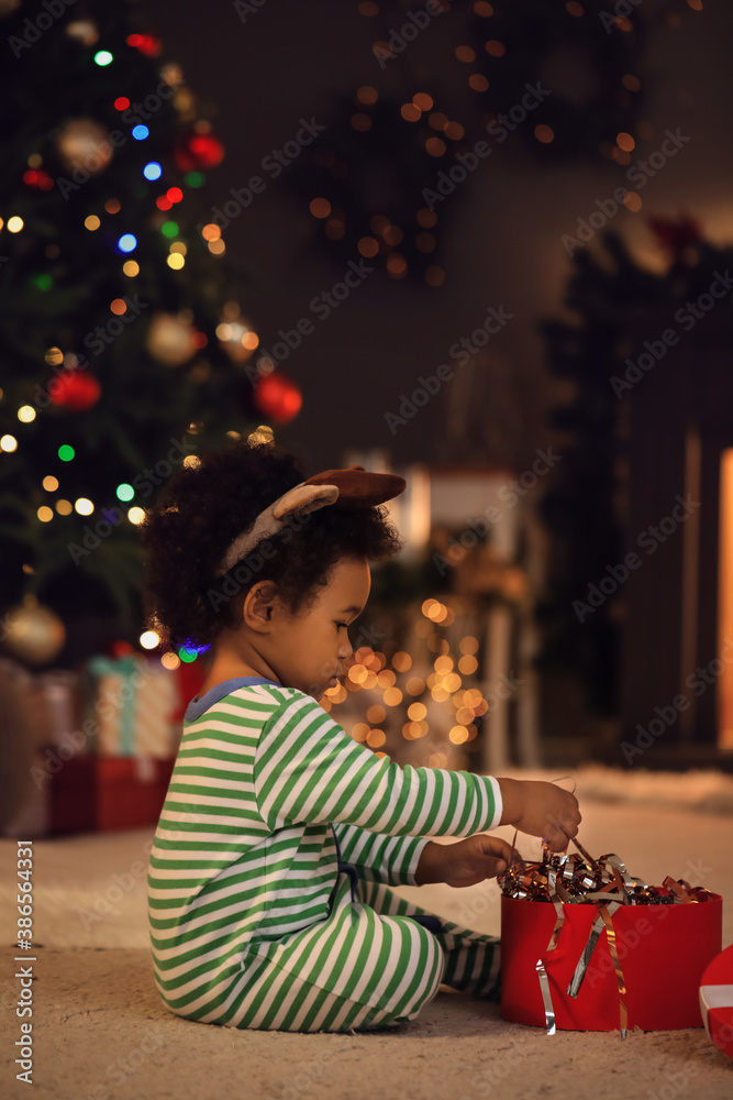 Cute African-American baby girl with gift at home on Christmas eve