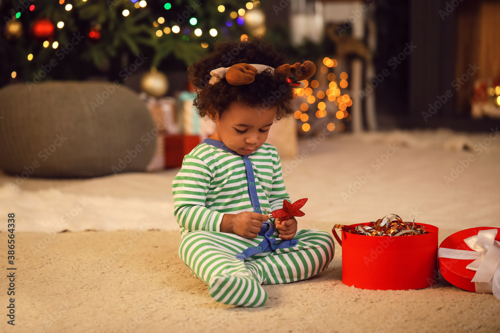 Cute African-American baby girl with gift at home on Christmas eve