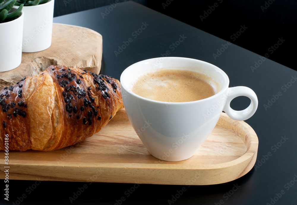 A cup of black coffee with a chocolate croissant for breakfast.