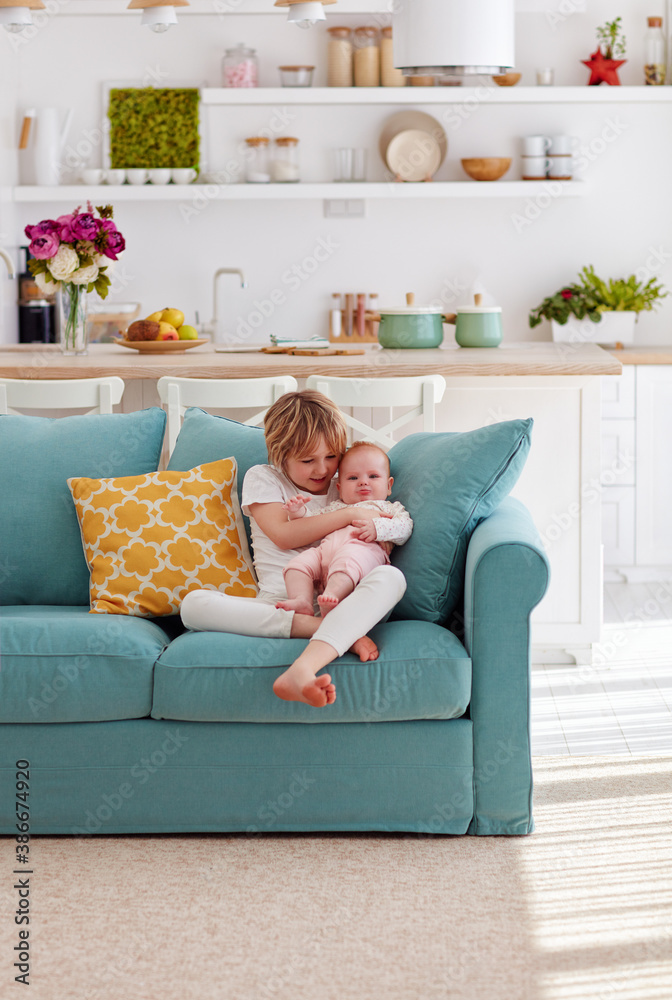 cute brother soothing sad little sister while sitting in cozy living room at home