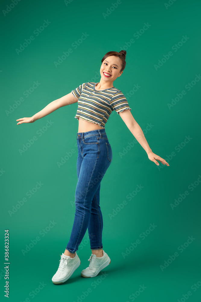 Full-length portrait of a happy young woman dancing on green background