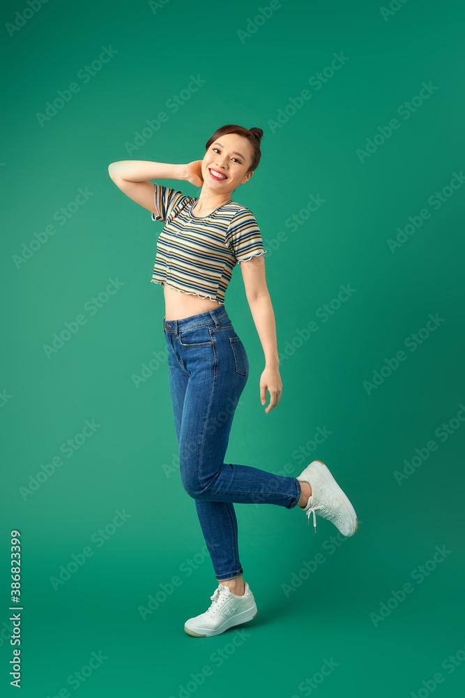 Joyful young Asian woman standing on one leg. Full length view of blissful girl dancing on green bac