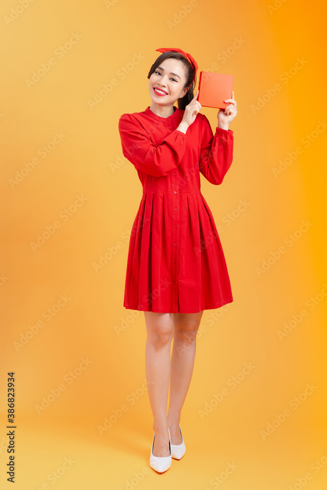 Happy young Asian woman showing gift box over orange background. Birthday, christmas, holiday, anniv