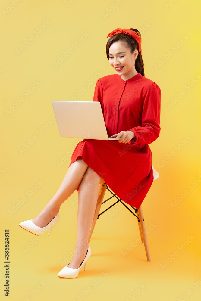 Full length portrait of a happy casual asian woman holding laptop computer while sitting on a chair 