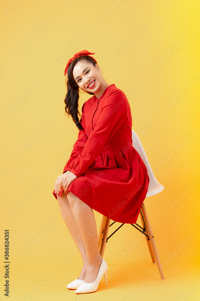 Attractive Asian girl sitting on modern chair isolated on orange background.