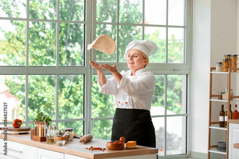 Mature female chef with dough for tasty pizza in kitchen