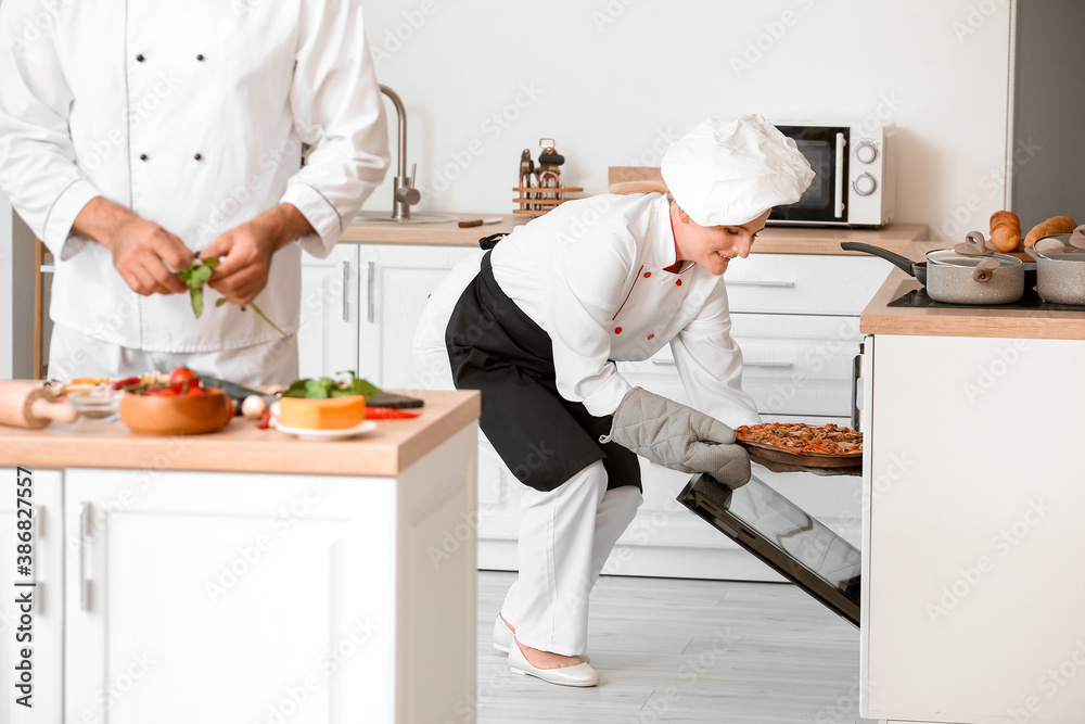 Chef taking tasty pizza from oven in kitchen