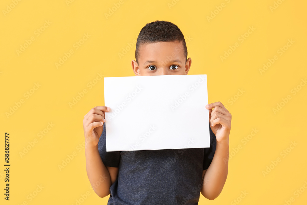 Little African-American boy with blank paper sheet on color background