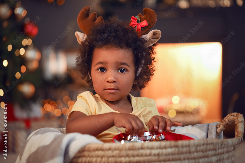 Cute African-American baby girl with gift at home on Christmas eve