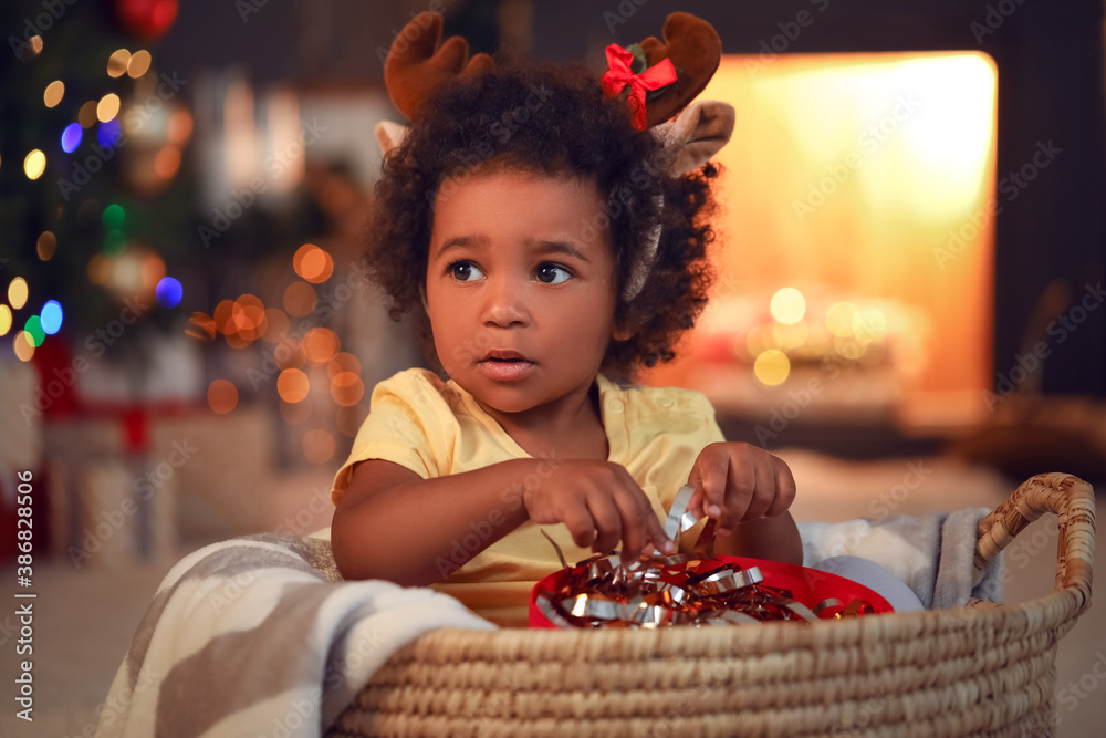 Cute African-American baby girl with gift at home on Christmas eve