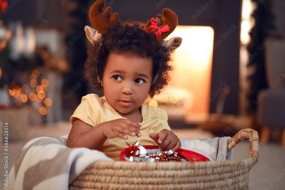 Cute African-American baby girl with gift at home on Christmas eve