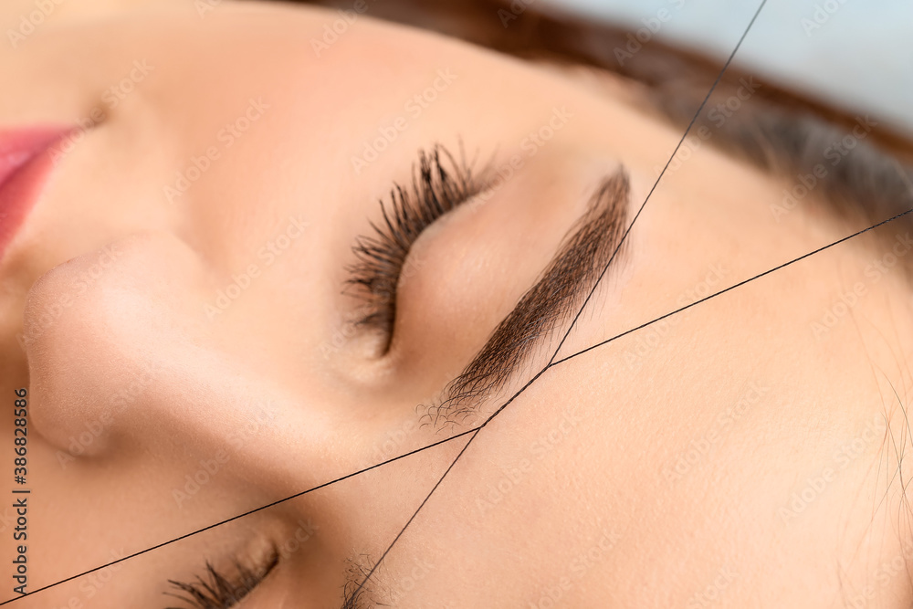 Young woman undergoing eyebrow correction procedure in beauty salon, closeup