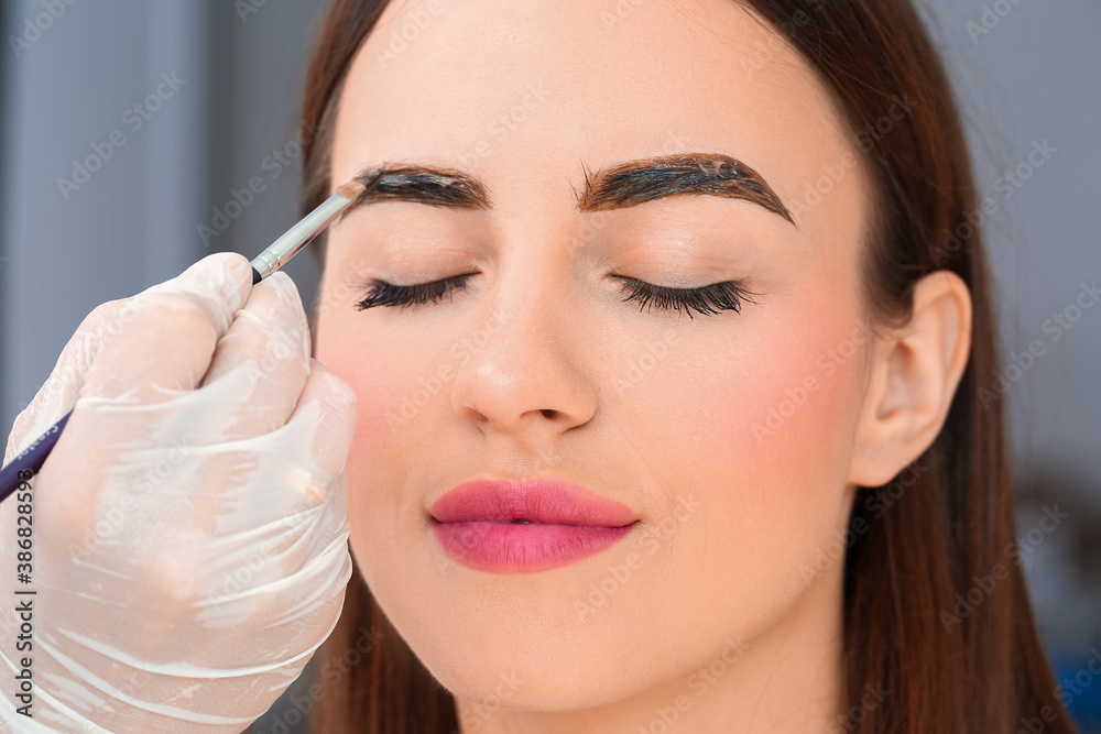 Young woman undergoing eyebrow correction procedure in beauty salon