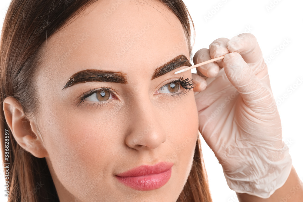 Young woman undergoing eyebrow correction procedure on white background