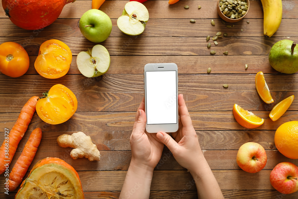 Female hands with mobile phone and fresh products on wooden background. Diet concept