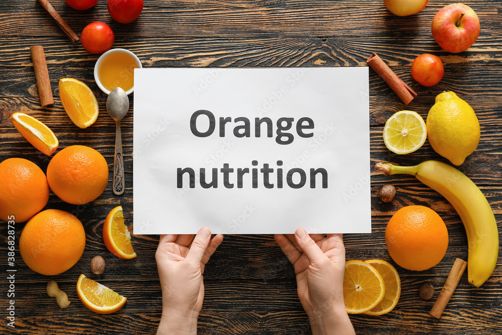 Female hands with text ORANGE NUTRITION on paper sheet and fresh products on wooden background