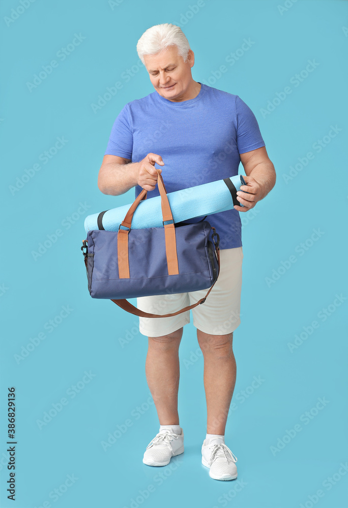 Sporty senior man with bag and yoga mat on color background