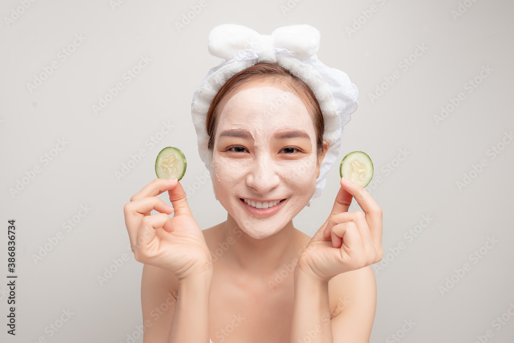 Cosmetic procedures. Woman with cosmetic mask on face eats cucumber slice.