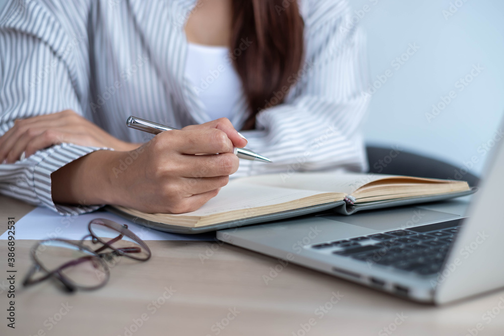 The hand of a student taking notes while studying online from their laptop.