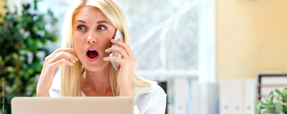 Surprised young woman talking on the phone in her home office