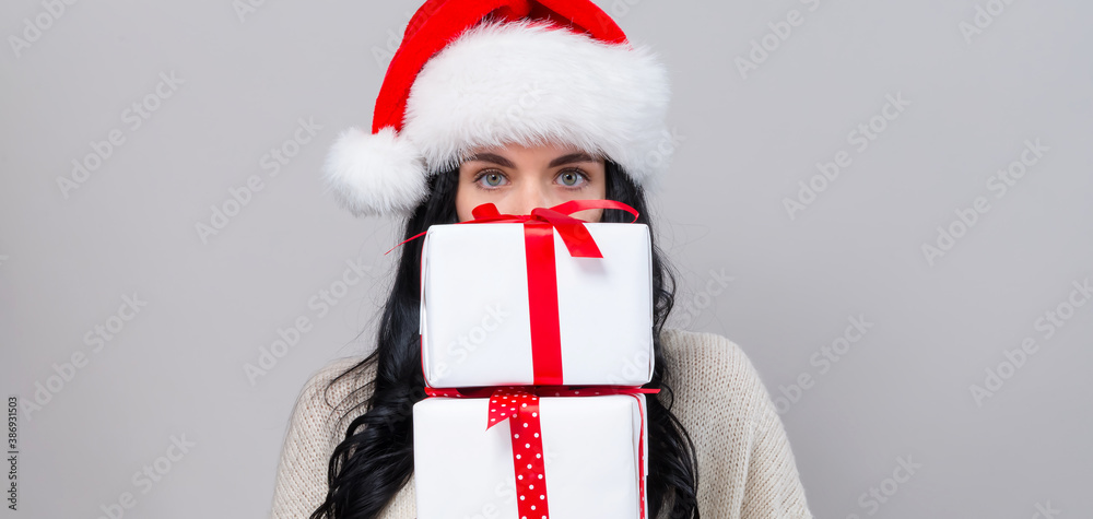 Young woman with santa hat holding gift boxes on a gray background