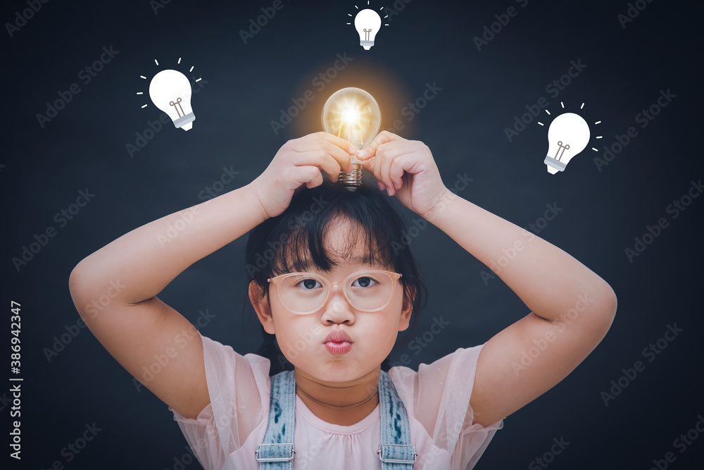 Happy little child wear glasses Has feelings happy holding light bulb over her head in the black bac