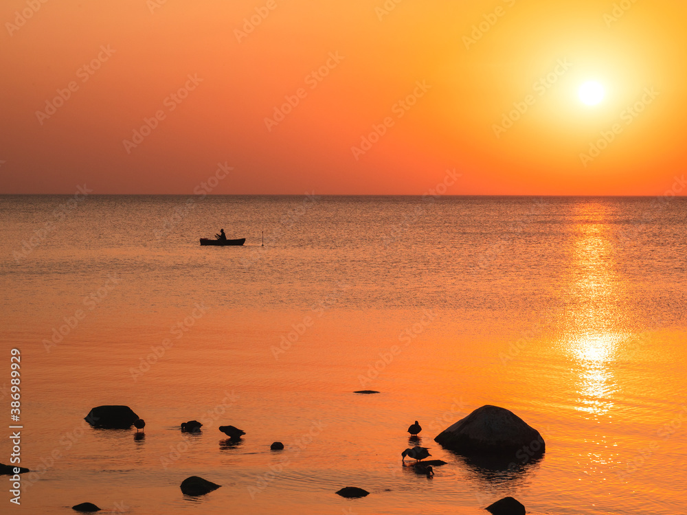 Beautiful sunset over rocky shore of sea with silhouettes of stones, birds and boat