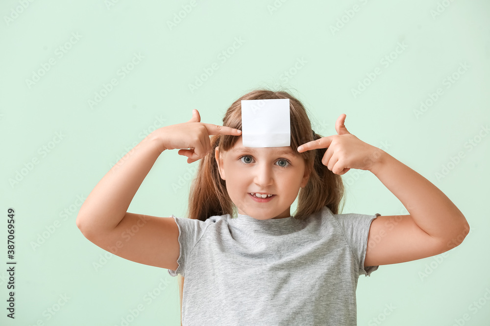 Little girl with blank note paper on her forehead against color background