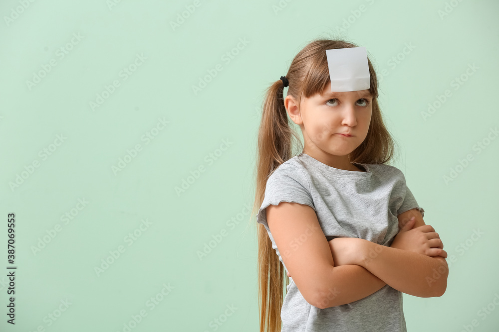 Displeased little girl with blank note paper on her forehead against color background