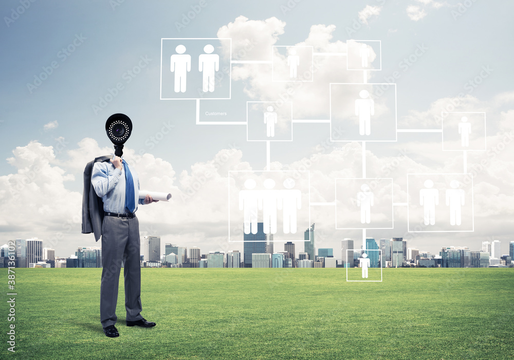 Camera headed man standing on green grass against modern cityscape