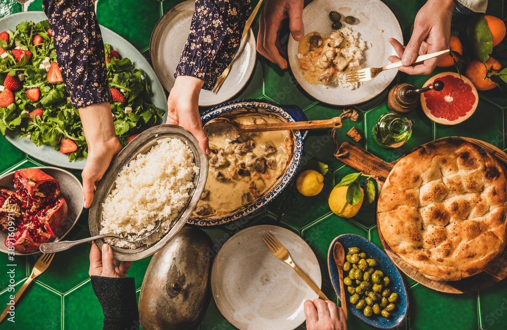 Family having Turkish dinner. Flat-lay of people passing rice pilav over green table with lamb in yo