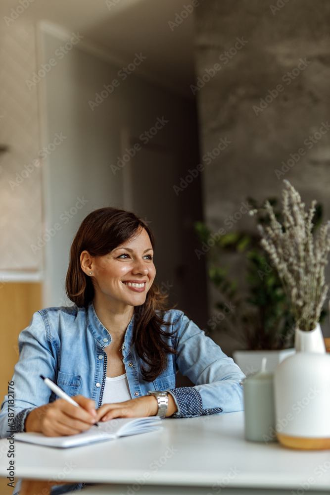 Woman looking around, while smiling and writing.