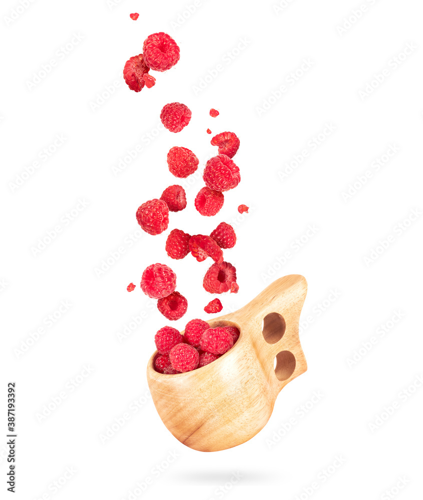 Raspberries fly out from a wooden cup on white background