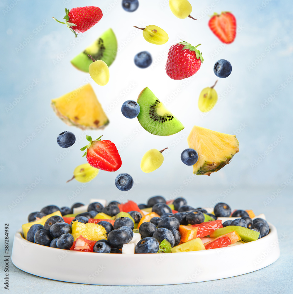 Plate with delicious fruit salad and flying ingredients on color background