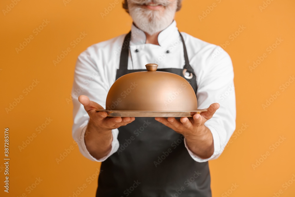 Mature male chef with tray and cloche on color background