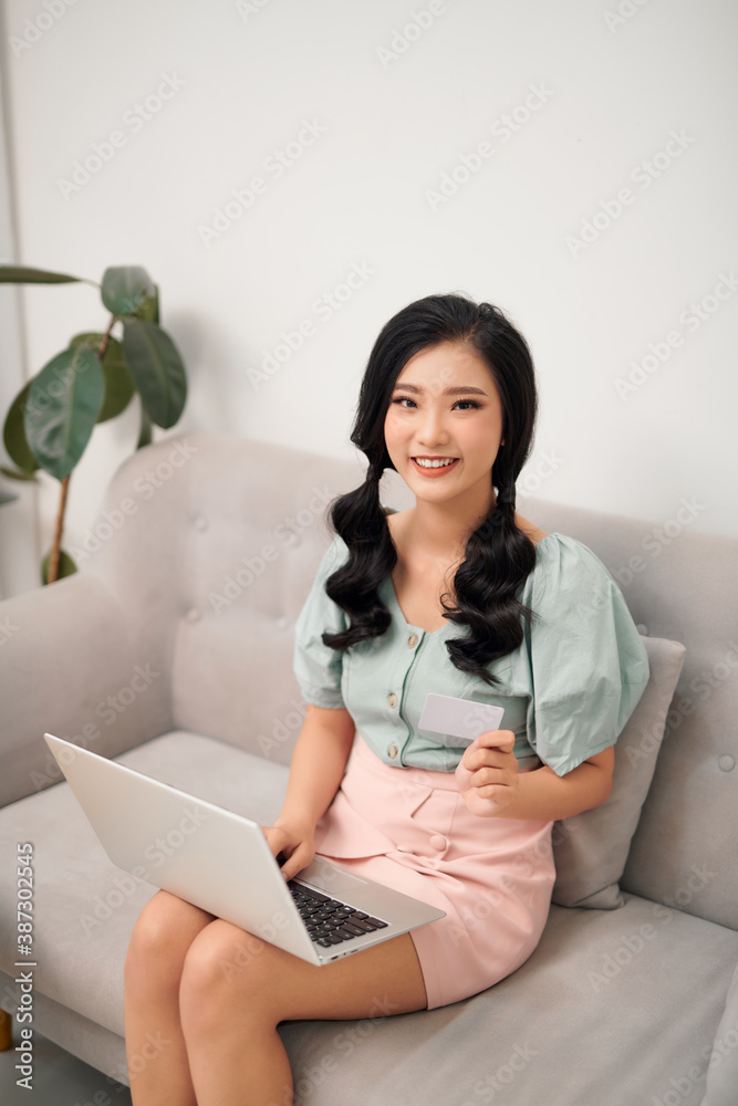 Portrait of young woman sitting in sofa buying something using credit card