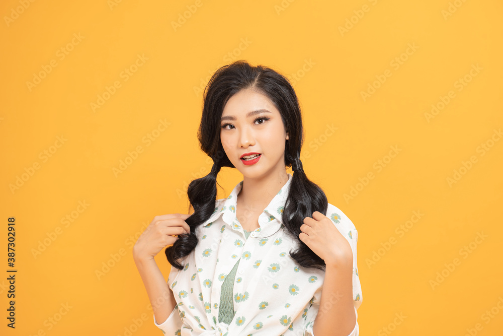 Happy asian woman in summer clothing posing and looking at the camera over yellow background