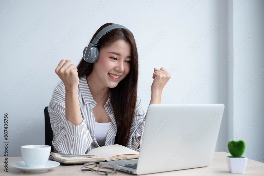 Young Asian women wear headphones using their laptop inside the office, working for online lessons o