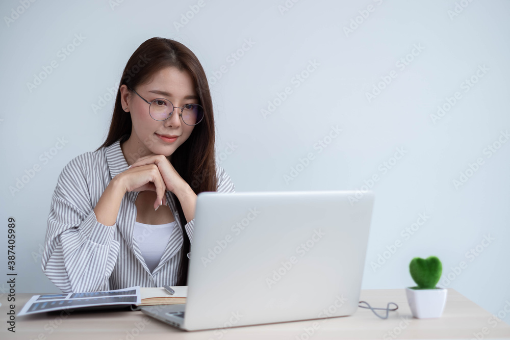 Portrait of a happy face Asian woman sitting at home working on a laptop while sitting on a desk. To