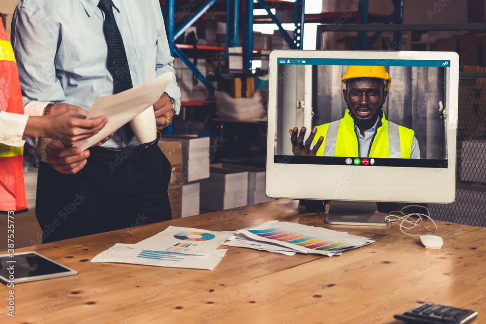 Warehouse staff talking on video call at computer screen in storage warehouse . Online software tech