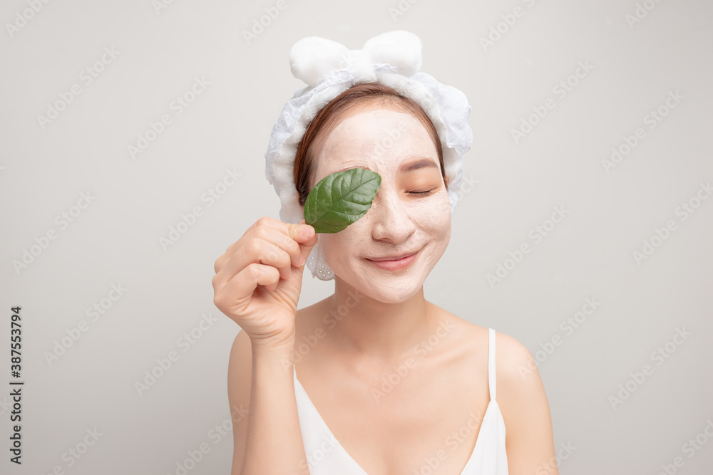 Beauty portrait of woman in towel on head with white nourishing mask or creme on face and green leaf