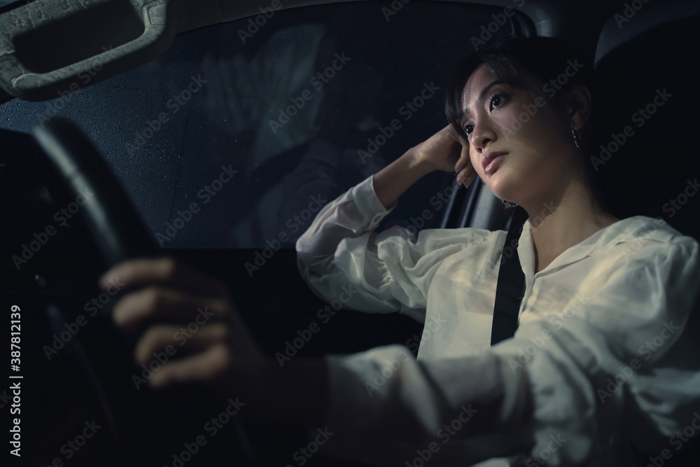 Asian woman is driving alone in the night. Its raining. She is stressed.