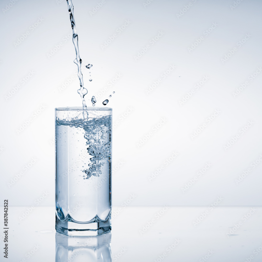 Fresh water pouring into glass on blue background