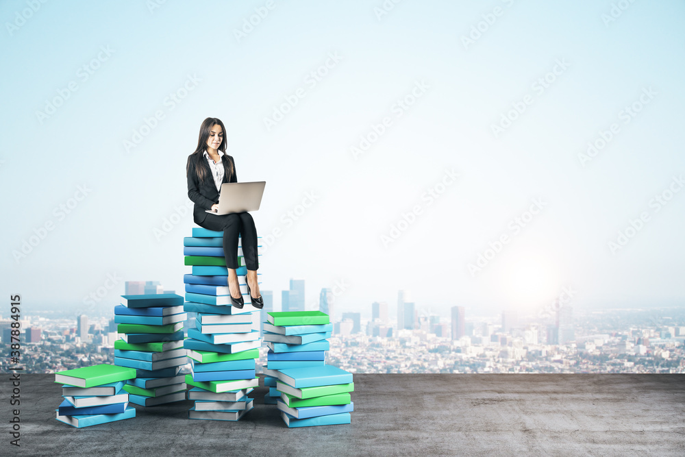 Young businesswoman with laptop computer sitting on books