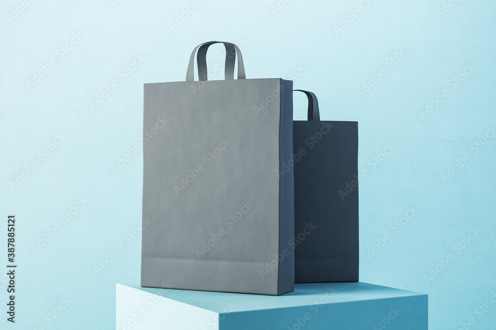 Two black paper shopping bag with handles on blue podium.