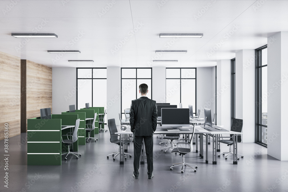 Businessman in suit standing in office interior with computers on green table.