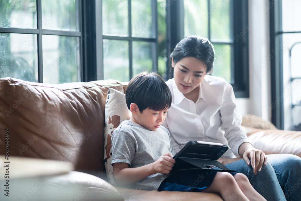 Asian mother teaching daughter learning online class on tablet.