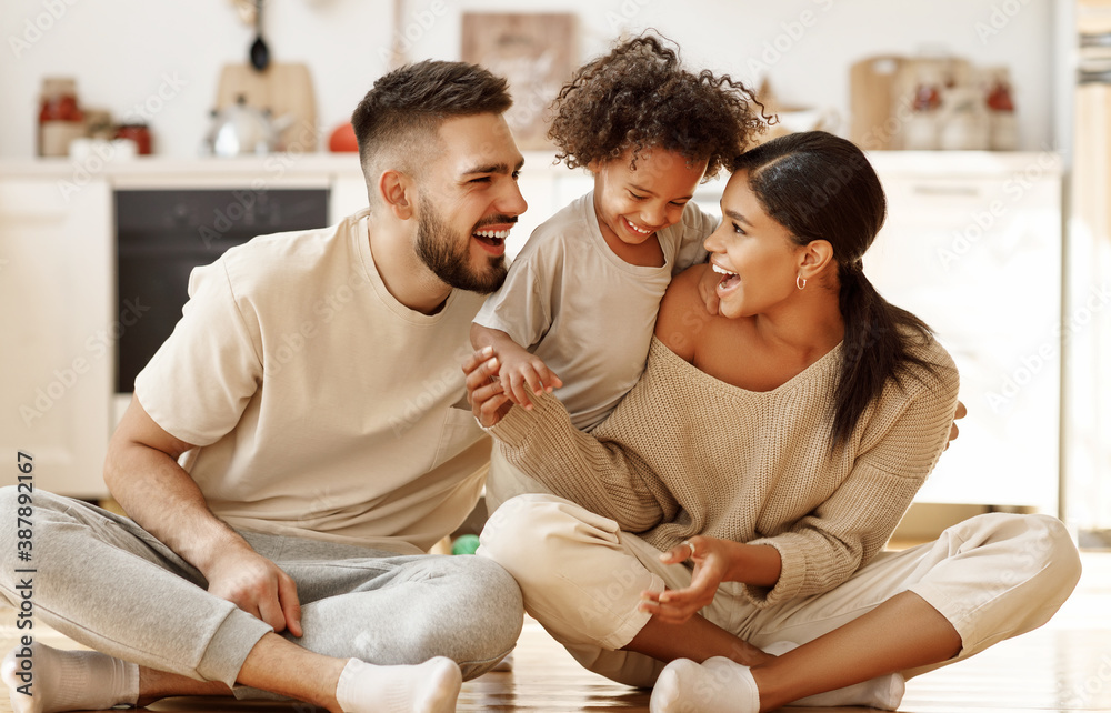 happy multiethnic family mom, dad and child  laughing, playing and tickles    on floor in cozy kitch